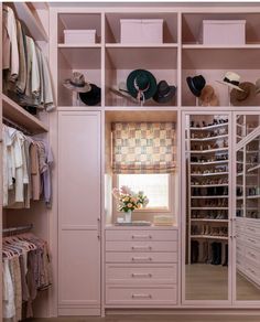 a walk in closet filled with lots of clothes and hats on top of shelves next to a window