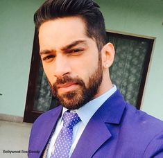 a man with a beard wearing a purple suit and blue polka dot tie looking at the camera