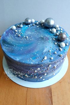 a cake with blue icing and silver balls on it sitting on a wooden table