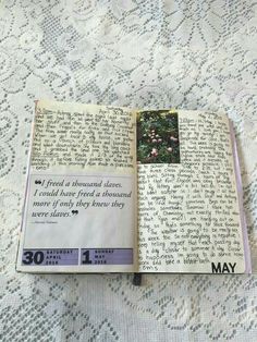 an open book sitting on top of a bed covered in white lacy material and writing