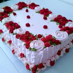 a heart shaped cake with white frosting and red roses on it's edges