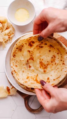 a person holding a tortilla on top of a white plate next to other food