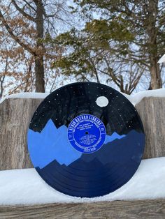 a record sitting on top of a wooden table covered in snow next to some trees