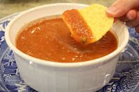 a person dipping a piece of bread into a bowl of tomato soup on a blue and white plate