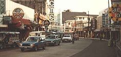 an old photo of cars parked on the side of the road in front of buildings