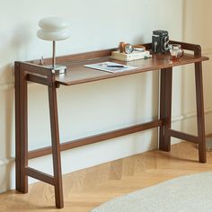 a wooden table with a lamp, camera and books on it in front of a white wall