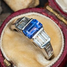 This gorgeous ring is centered with one (1) emerald cut tanzanite set into a channel. The ring is also accented with sixteen (16) baguette cut diamonds set into channels. The ring measures 6.8mm at the top, rises 5.5mm above the finger, tapering to 2.4mm wide and 1.0mm thick at the base of the shank. This ring is currently a size 5. Luxury Tanzanite Rings With Tension Setting, Emerald Cut Sapphire Ring With Baguette Diamonds, Luxury Tanzanite Diamond Ring With Emerald Cut, Classic Tanzanite Emerald Cut Diamond Ring, Gia Certified Baguette Cut Tanzanite Ring, Emerald Cut Tanzanite Diamond Ring, Gia Certified Tanzanite Emerald Cut Rings, Tanzanite Gemstone Ring In Baguette Cut, Channel Set Sapphire Rings With Emerald Cut