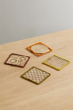 four woven coasters sitting on top of a wooden table next to an orange vase