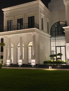 a large white house lit up at night with lights on the windows and balconies