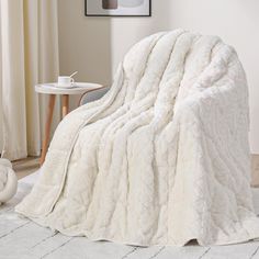 a large white blanket sitting on top of a bed next to a table and chair