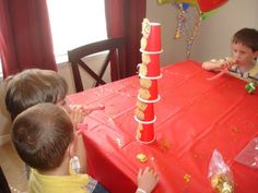 three children sitting at a red table with balloons and confetti on top of it