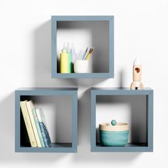 three square shelves with books, cups and other items on them against a white wall