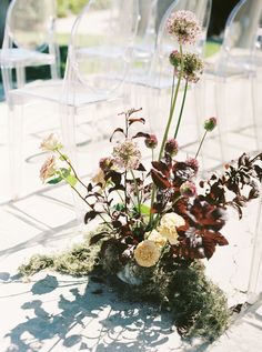 an arrangement of flowers and greenery on the ground in front of clear acrylic chairs