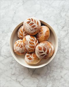 a bowl filled with croissants covered in powdered sugar on top of a marble counter