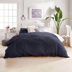 a bedroom with white walls and blue comforter on the bed, along with potted plant