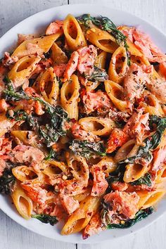 a white bowl filled with pasta and meat covered in sauce on top of a wooden table