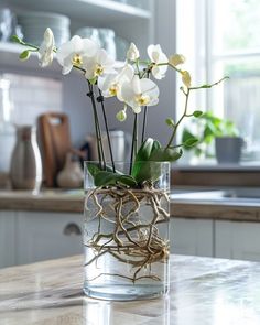 some white flowers are in a glass vase on the counter top with water and twigs