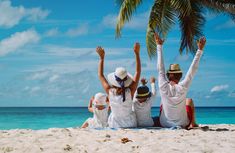 three people sitting on the beach with their arms in the air