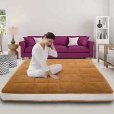 a woman sitting on top of a brown rug in front of a purple couch and coffee table