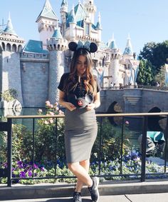 a woman is standing in front of a castle with mickey mouse ears on her head