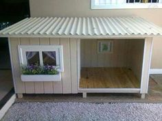 a dog house made out of wood with a white roof and flower boxes in the window