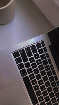 an open laptop computer sitting on top of a white desk next to a coffee cup