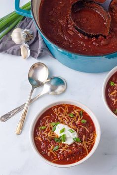 two bowls of chili with sour cream on top and spoons next to the bowl