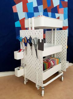 a white shelf with scissors and other crafting supplies on it in front of a colorful wall