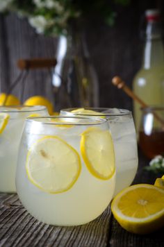 three glasses filled with lemonade sit on a table next to some sliced lemons