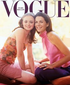 two women are sitting on the bed posing for a photo together, one is wearing a pink top and the other has a striped skirt