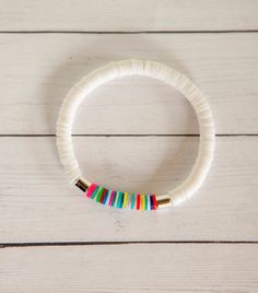 a white bracelet with multicolored beads on top of a wooden table next to a cell phone