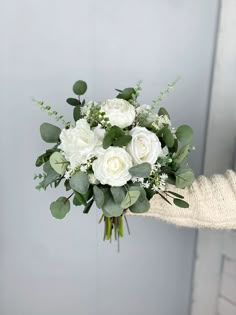 a bouquet of white roses and greenery in someone's hand