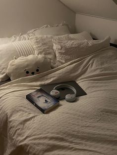 there is a book and headphones on top of the bed with white sheets in this room