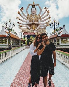 a man and woman standing in front of a large buddha statue with their arms around each other