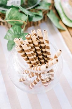 striped paper straws in a glass bowl on a table with greenery behind them