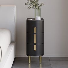 a black and gold side table with a vase on it next to a white couch