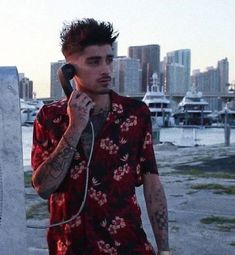 a man with tattoos on his arm talking on a cell phone while standing next to the water