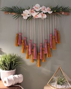 a wall hanging with flowers and tassels on it next to a potted plant