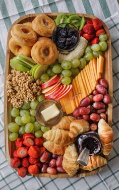 a wooden platter filled with different types of fruit and pastries on top of a checkered table cloth