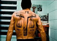 a man with his back turned to the camera, holding a cross and scale tattoo