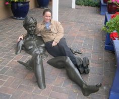 a woman sitting on the ground next to a statue with her legs spread out,