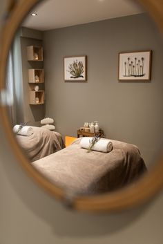 a mirror reflecting two massage beds in a room with pictures on the wall behind them