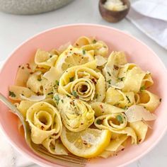 a pink bowl filled with pasta and lemon slices