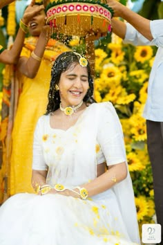 a woman in white dress sitting on the ground with yellow flowers around her head and two men standing behind her