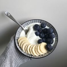 a person holding a bowl of yogurt and blueberries with a spoon in it