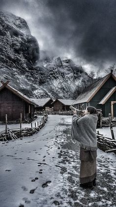 a man standing in front of a mountain with snow on the ground and houses behind him