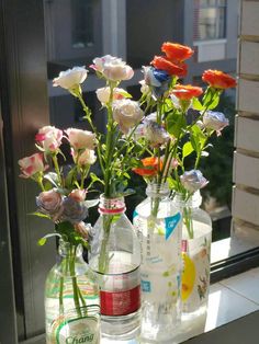 three bottles with flowers in them sitting on a window sill next to each other