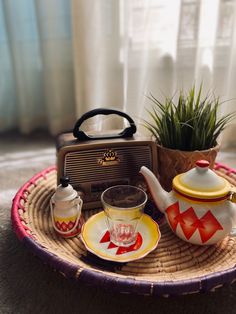 a tea set on a wicker tray with a radio and potted plant in the background