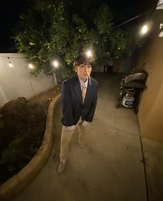 a man in a suit and tie standing on a sidewalk at night with his head turned to the side