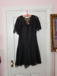 "Absolutely stunning dress! This is likely from the 1930's (possibly 20's) and is made of two layers of black silk. The outer layer is sheer and very delicate. This dress has a dropped waist and slightly asymmetrical flounce hem. There is a saw tooth capelet /sleeves attached and a sweet little pink floral bouquet and bow pinned to the neckline. Looks like it has thread loops for a ribbon belt or sash, but they are popped. No label on this beauty. Overall the dress is in good condition for it's Vintage Silk Flapper Dress, Vintage Silk Flapper Dress Fitted, Vintage Silk Fitted Flapper Dress, 1920s Fitted Flapper Dress For Vintage Events, Elegant Fitted Flapper Dress For Costume, 1920s Fitted Flapper Dress For Formal Occasions, Victorian Style Fitted Vintage Costume Dress, Fitted Vintage Flapper Dress For Vintage Events, Vintage Black Flapper Dress For Formal Occasions